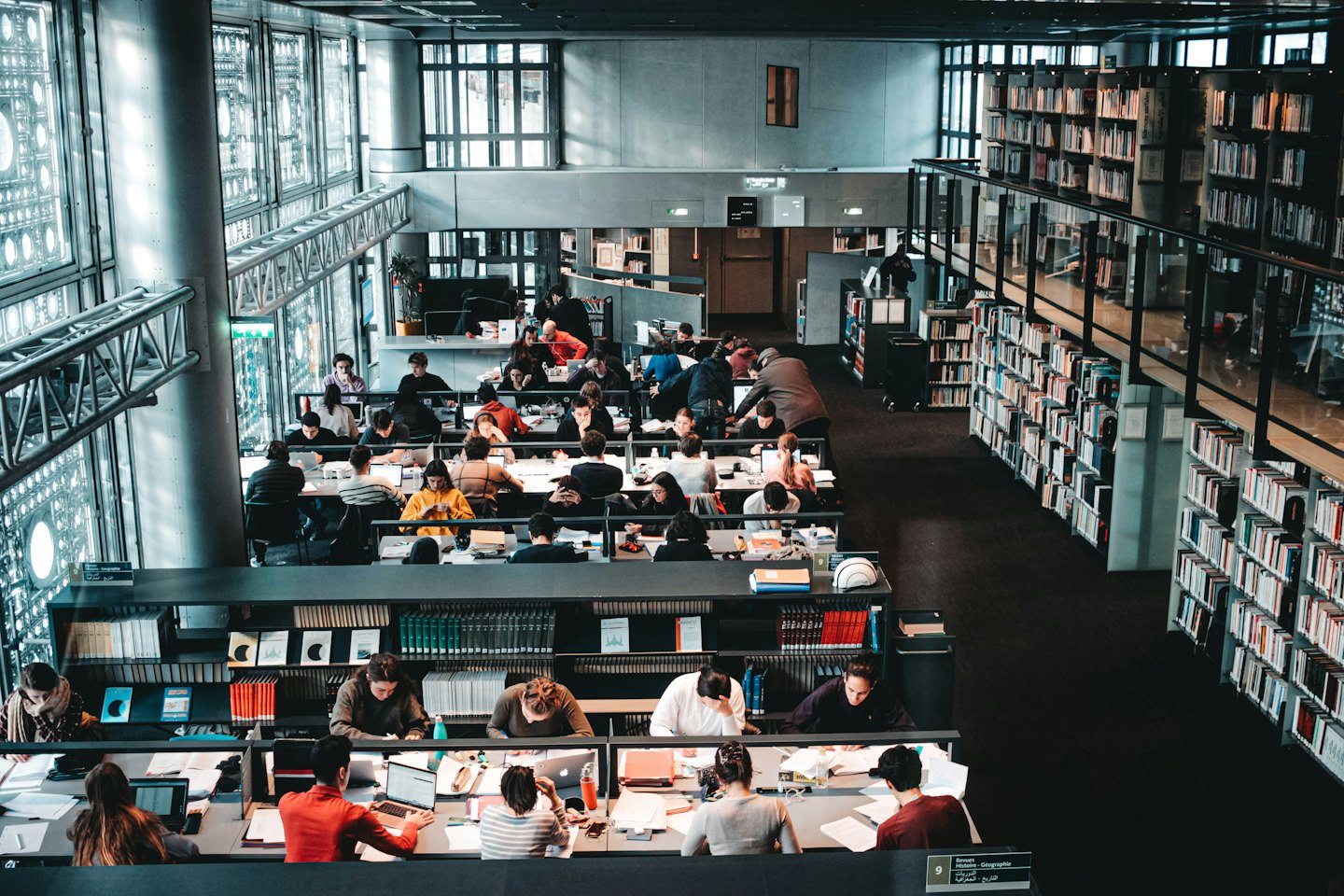 Personas estudian y trabajan en mesas en una gran biblioteca.